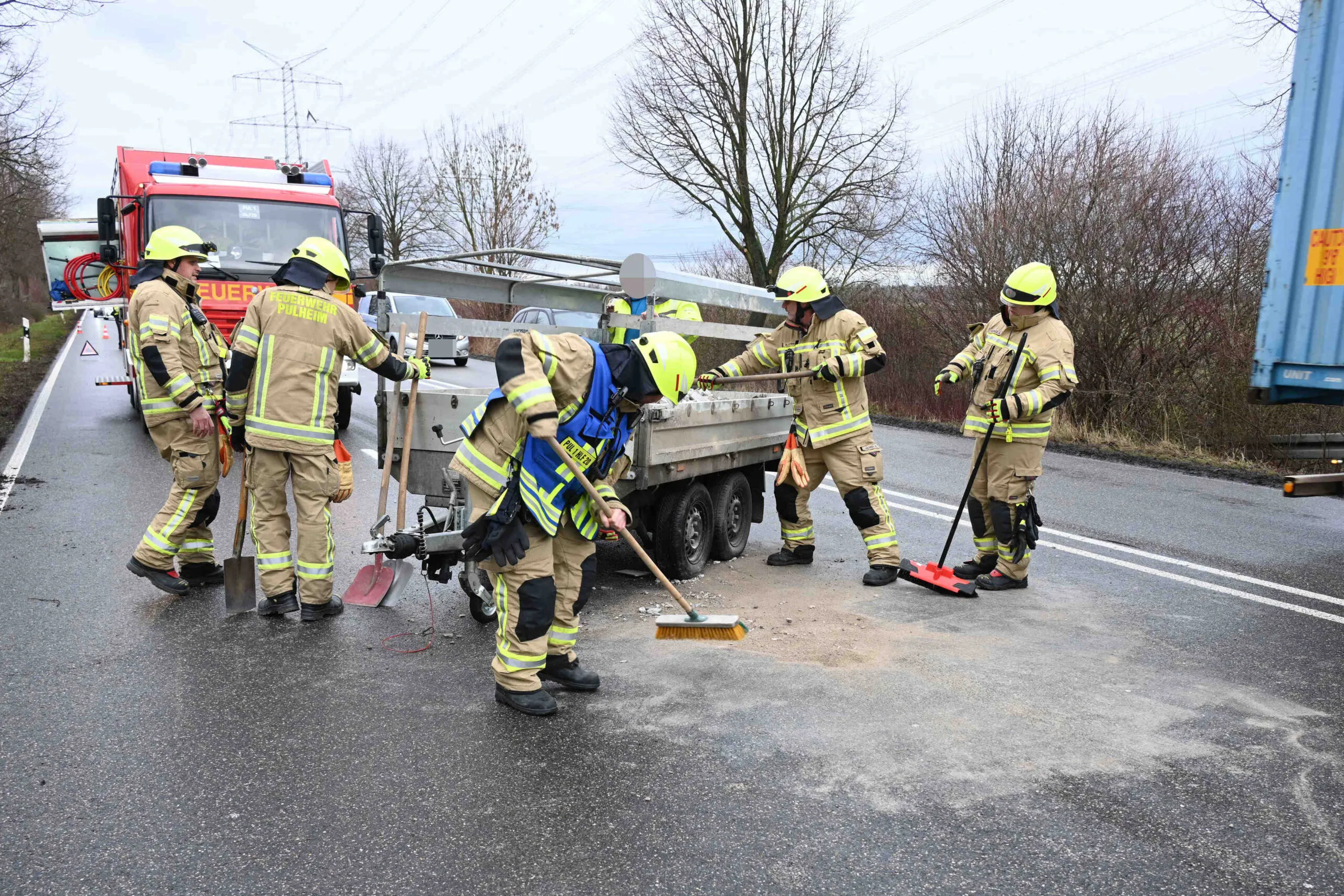 Einsatzkräfte der Feuerwehr Pulheim richten einen umgekippten Anhänger auf der Bundesstraße 59 wieder auf und räumen ausgelaufenen Bauschutt von der Fahrbahn.